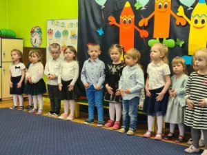 Dzieci stoją w rzędzie i śpiewają piosenkę.