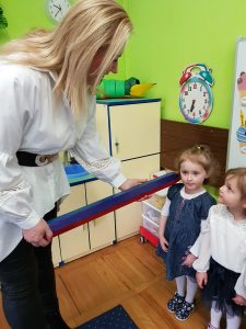 Pani Dyrektor przykłada dziecku do ramienia dużą, drewnianą kredkę.