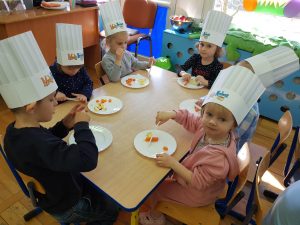 Dzieci w czapkach kucharza kroją marchewki i jabłka