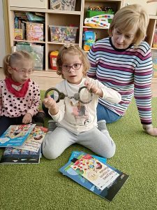 2 Dziewczynki i Pani. Jedna dziewczynka trzyma w rękach kajdanki.