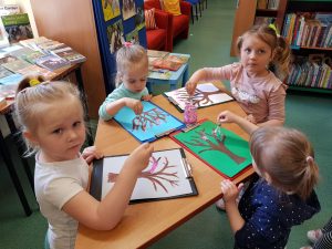 4 dzieci stoi przy stoliku i maluje za pomocą złączonych patyczków.