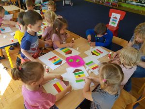 Dzieci przy stoliku wykonują pracę plastyczną.
