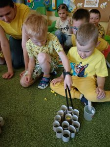 Chłopiec szczypcami wrzuca pompony do papierowego plastra miodu.