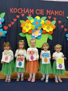 Dziewczynki w kolorowych spódniczkach trzymaja prace plastyczne w rękach