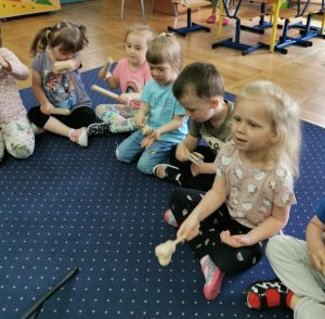 Dzieci siedza na dywanie i grają na instrumentach.