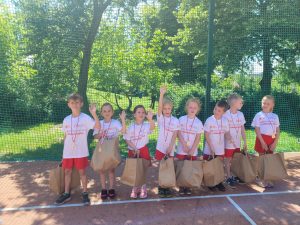 Ośmioro dzieci stojących w jednym rzędzie ubranych w stroje sportowe, majace na szyi zawieszone medale, trzymajace papierowe torby.