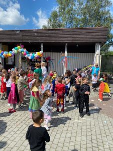 Grupa dzieci uczestnicząca w grach i zabawach ruchowych przed budynkiem przedszkola.