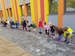 Dzieci na dworze stoją w rzędzie i dotykają swoich kolan.