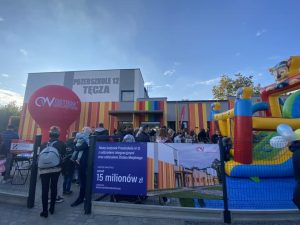 Budynek przedszkola , przed nim rodzice i dzieci, dmuchany zamek, duży balon z napisem Ostrów Wielkopolski
