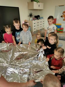 Grupa dzieci trzyma w rękach i ogląda ratunkowy koc termiczny