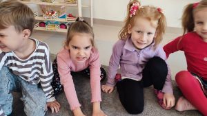 Dziewczynka w bluzie różowej i fioletowej pokazuje złość, obok chłopiec w bluzie w paski.