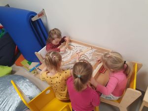 Cztery dziewczynki siedzące przy stoliku, bawiace sie piaskiem kinetycznym.