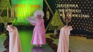Dziewczynka z róźowej sukni balowej z wachlarzem w ręce i peruką.