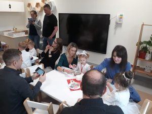 Dzieci z rodzicami siedzą przy stolikach i ozdabiają pierniki.