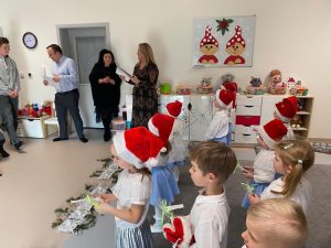 Dzieci stoją na wprost rodziców w rękach trzymają prezenty. Z boku stoją dwie kobiety, jedna ubrana na czarno, druga na brązowo. Obok nich mężczyzna w niebieskiej bluzce, który w rękach trzyma dyplom.