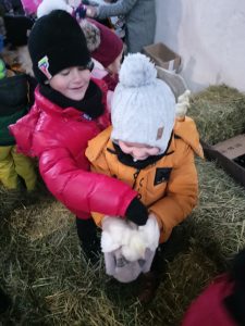 Chłopiec trzyma w rękach małego kurczaczka, kolega obok leciutko go dotyka.