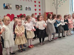 Zdjęcie przedstawia dzieci podczas występu, dzieci ubrane są elegancko - w białe koszule a dziewczynki w sukienki.
