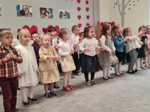Zdjęcie przedstawia dzieci podczas występu, dzieci ubrane są elegancko - w białe koszule a dziewczynki w sukienki