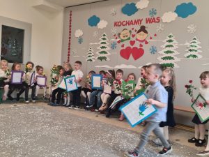 Dzieci trzymają w rękach laurki i róże dla babci i dziadka