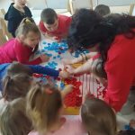 DZIECI Z NAUCZYCIELEM WYKLEJAJĄ SERCE Z NAKRĘTEK