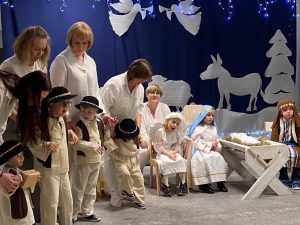 Przebrane Dzieci siedzą na krzesełkach obok stoją chłopcy przebrani za pasterzy. Za nimi stoją Panie
