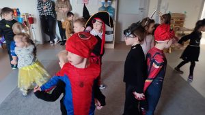 Chłopcy w strojach Batmana, Spider Men, Pirat i inne dzieci tańczą na szarym dywanie.
