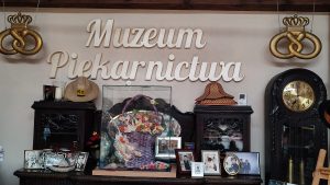 Na szarej ścianie widnieje napis Muzeum Piekarnictwa. Pod napisem na kredensie stoją stare eksponaty. zdjęcia rodziny Vogt.
