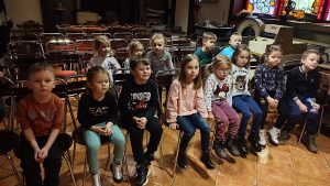 Grupa dzieci siedzi na krzesłach i ogląda film edukacyjny o chlebie.