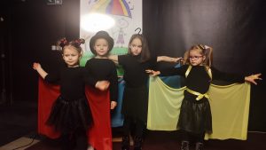 Cztery dziewczynki ubrane na czarno z kolorowymi elementami skrzydeł.