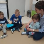 Dzieci siedzą w kole. Podają sobie niebieskie papierowe serce, za pomocą klamerek trzymanych w rączkach.