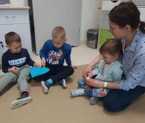 Dzieci siedzą w kole. Podają sobie niebieskie papierowe serce, za pomocą klamerek trzymanych w rączkach.