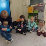 Dzieci siedzą w kole. Podają sobie niebieskie papierowe serce, za pomocą klamerek trzymanych w rączkach.