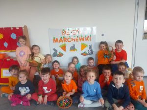 ZDJĘCIE GRUPOWE NA TLE TABLICY Z NAPISEM DZIEŃ MARCHEWKI