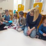 Dzieci siedzą w kole. Podają sobie niebieskie papierowe serce, za pomocą klamerek trzymanych w rączkach.