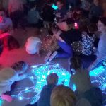 Dzieci dotykają niebieskich światłowodów, które są rozłożone na dywanie.