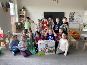 Dzieci siedzą na dywanie z prezentem od zajączka
