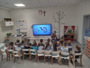 DZIECI OGLĄDAJĄ FILM DOKUEMNTALNY O DELFINACH NA TABLICY MULTIMEDIALNEJ
