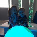 Dziewczynka i chłopiec siedzą uśmiechnięci, trzymając podświetloną na niebiesko Kulę Ziemską.