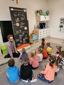 Pan astronom opowiada dzieciom siedzącym na dywanie o kosmosie