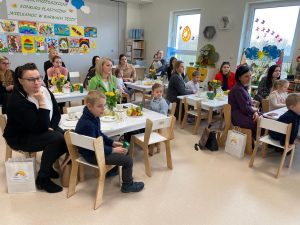 Panie nauczycielki i dzieci siedzące przy stolikach oglądające występ dzieci