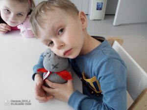 Chłopiec ubrany w niebieska bluzę przytula się do małego zajączka zrobionego z skarpetki.