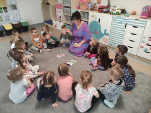 Dzieci i nauczycielka siedzą w kole na dywanie