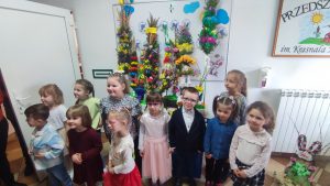 Dzieci stoją na tle palm wielkanocnych. Wszystkie dzieci brały udział w konkursie.