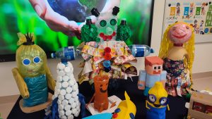 Na granatowym materiale stoją zabawki wykonane z odpadów kartonowych, plastikowych itd.