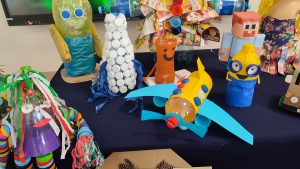 Na granatowym materiale stoją zabawki wykonane z odpadów kartonowych, plastikowych itd.