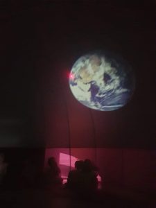 Różowe tło kopuły planetarium, na którym widać obraz kuli ziemskiej.