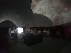 Szare tło kopuły, dzieci siedzą na podłodze i oglądają ziemię i kosmos.