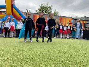 3 dzieci ubranych na czarno z kolorowymi chustami stoją na zielonym dywanie i mówią życzenia rodzicom.