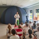 Dzieci słuchające pana astronoma stojącego na tle planetarium