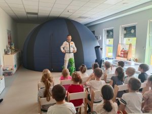 Dzieci słuchające pana astronoma stojącego na tle planetarium